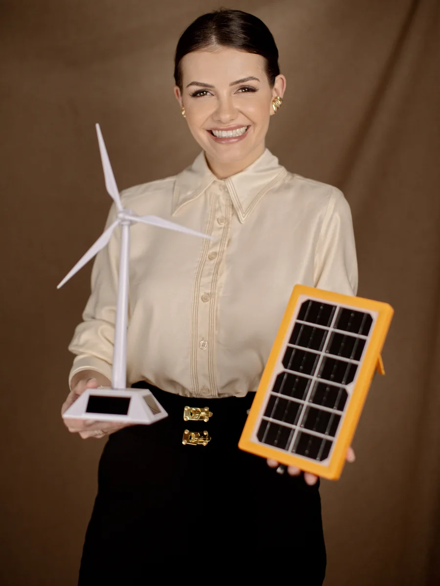 Engª Joiris Manoela Dachery, a Joi, segurando uma miniatura de turbina eólica e uma placa solar